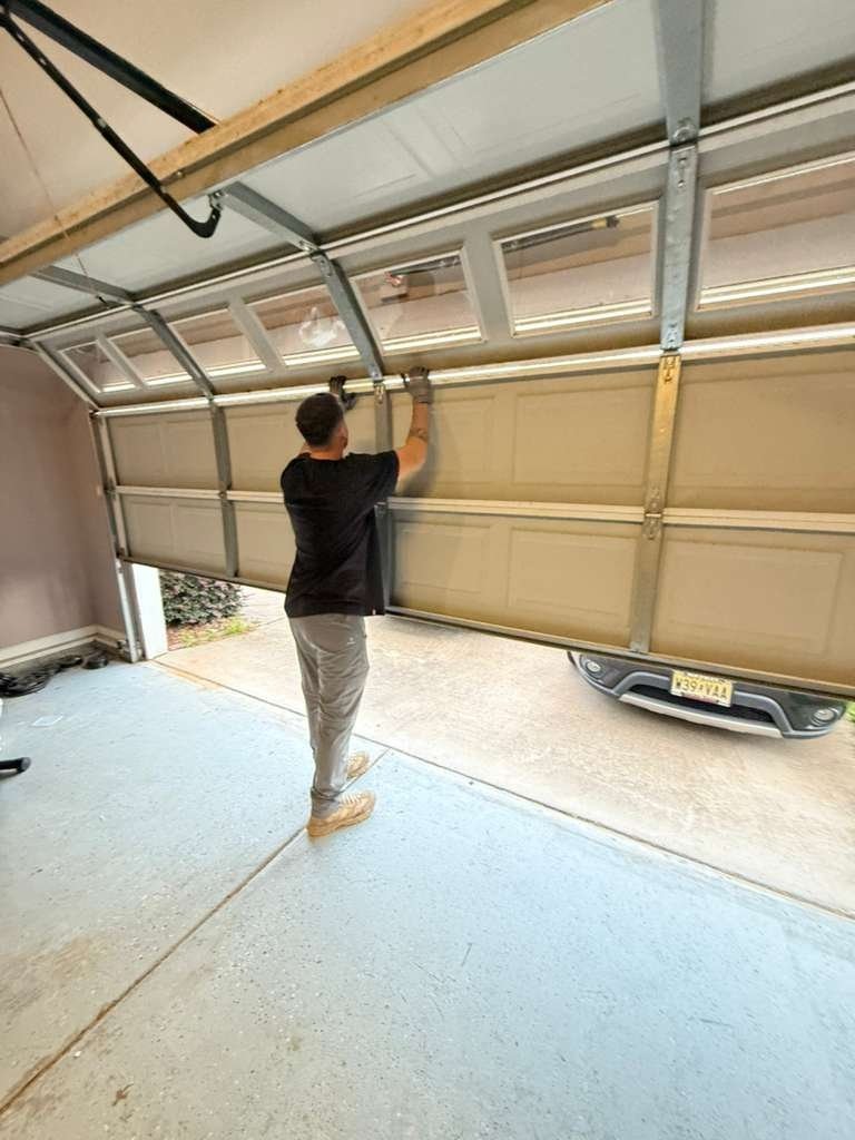 Worker standing inside an open garage checking overhead door hardware