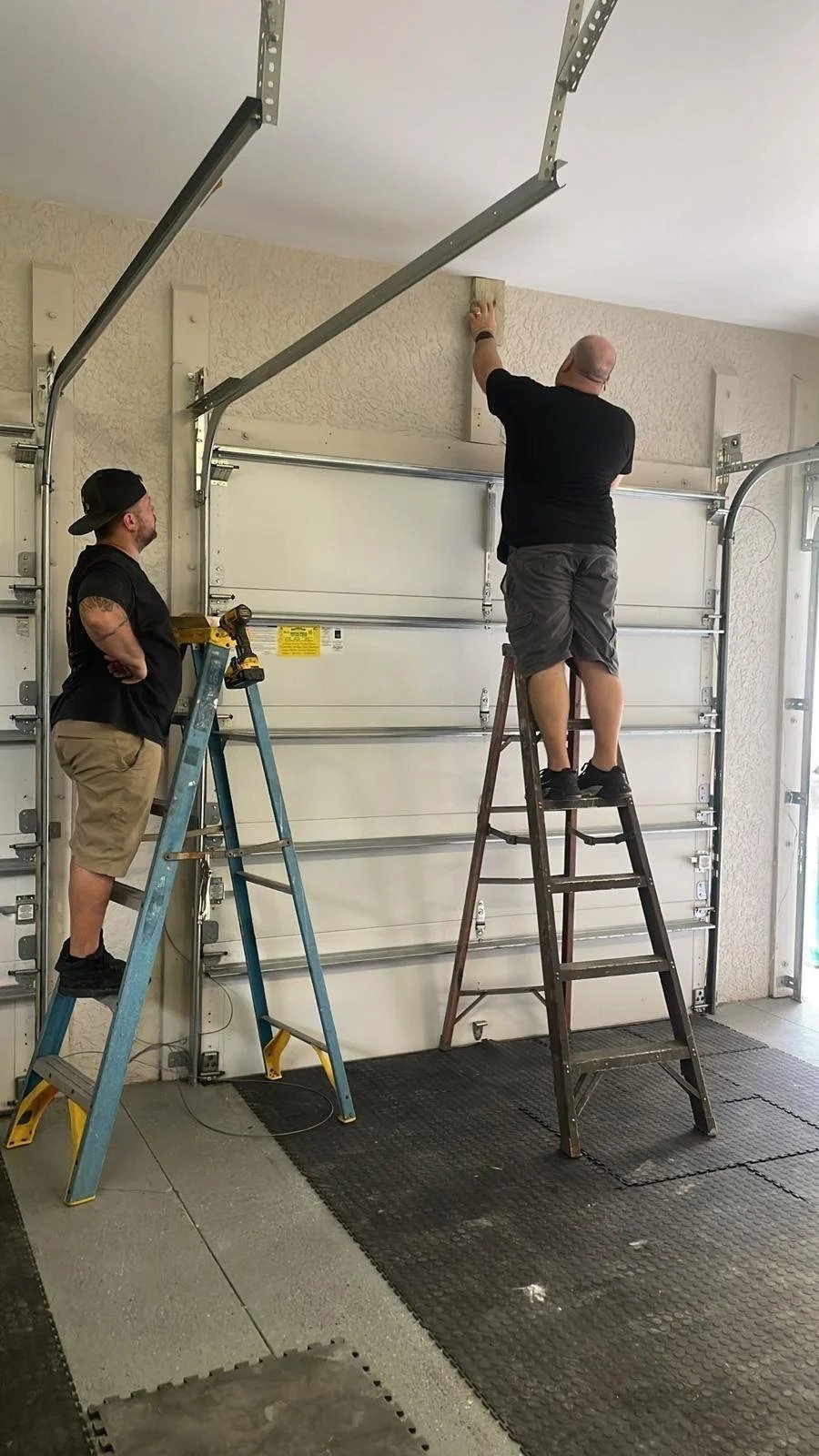 Two workers on ladders beside the upper panel of a sectional door