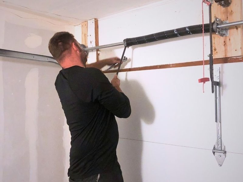 Worker inspecting the torsion spring shaft above a white door